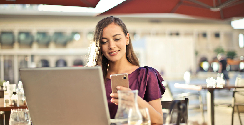 Woman checking phone while working on laptop in plaza